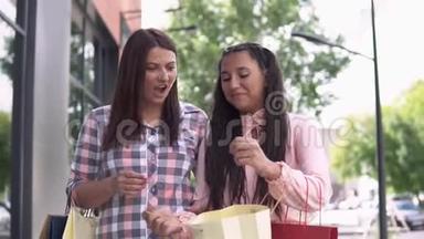 两个穿着漂亮衣服的漂亮女孩拿着购物袋在商场附近购物后去。 慢动作。 高清高清